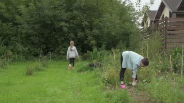 Anne ve kız bahçede çalışıyor, arka bahçedeki bitkilerle ilgileniyor, yatakları hasat ediyor ve yabani otları temizliyor.