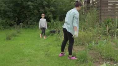 Anne ve kız bahçede çalışıyor, arka bahçedeki bitkilerle ilgileniyor, yatakları hasat ediyor ve yabani otları temizliyor.