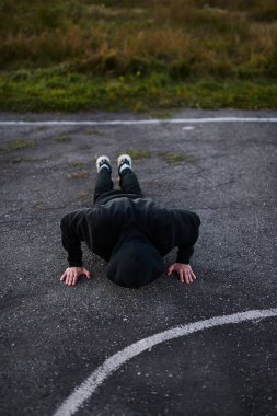 Siyah spor kıyafetli genç adam spor sahasında şınav çekiyor.