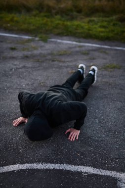 Siyah spor kıyafetli genç adam spor sahasında şınav çekiyor.