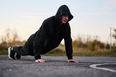 Siyah spor kıyafetli genç adam spor sahasında şınav çekiyor.