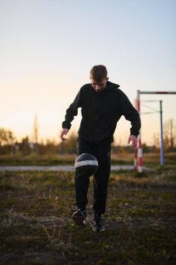 Siyah spor giyimli genç adam spor sahasında futbol oynuyor.