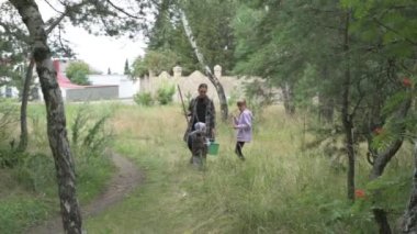 Çocuklu anne ormanda yürüyor, mantar, böğürtlen ve ot topluyor.