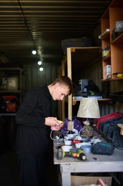 Garajda elektrikli aletlerle çalışan, bir şeyleri tamir eden genç bir adam.