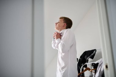 Bir öğrenci okula gitmek için hazırlanıyor. Üniforma giyiyor, beyaz gömlek giyiyor.