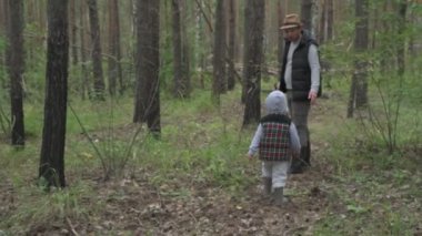 Baba ve oğul yeşil bir ormanda yürürler, mantar ve böğürtlen toplarlar.