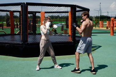 Genç adam ve kadın çift boks antrenmanı, kum torbasına vurmak, spor sahasında spor yapmak.