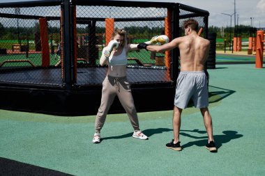 Genç adam ve kadın çift boks antrenmanı, kum torbasına vurmak, spor sahasında spor yapmak.