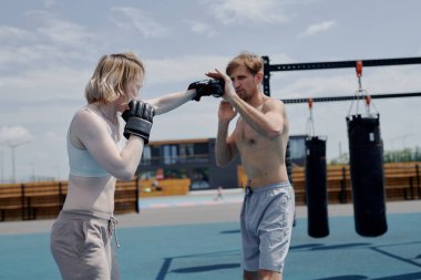 Genç adam ve kadın çift boks antrenmanı, kum torbasına vurmak, spor sahasında spor yapmak.