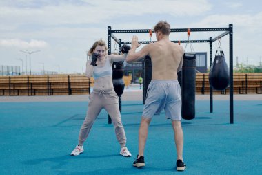 Genç adam ve kadın çift boks antrenmanı, kum torbasına vurmak, spor sahasında spor yapmak.