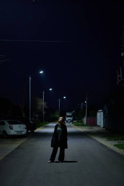 Siyah elbiseli genç bir kızın portresi bir gece şehrinin arka planında duygusuz bir yüz ifadesi.