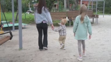 Çocuklu anne, erkek ve kız, parkta yürüyor, kum havuzunda oynuyor ve salıncakta sallanıyor.