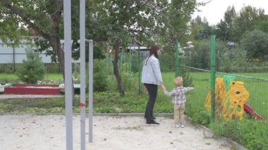 Anne ve küçük oğlu parkta yürüyor, kum havuzunda oynuyor ve salıncakta sallanıyor.