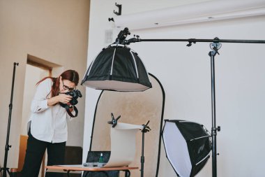 Kadın fotoğrafçı, arka plandaki objelerin fotoğrafını çekiyor. Profesyonel ekipmanlarla birlikte.