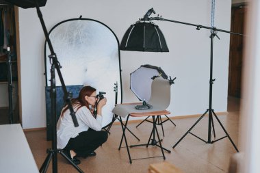 Kadın fotoğrafçı, arka plandaki objelerin fotoğrafını çekiyor. Profesyonel ekipmanlarla birlikte.
