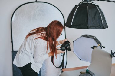 Kadın fotoğrafçı, arka plandaki objelerin fotoğrafını çekiyor. Profesyonel ekipmanlarla birlikte.