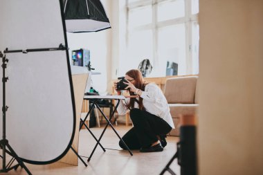 Kadın fotoğrafçı, arka plandaki objelerin fotoğrafını çekiyor. Profesyonel ekipmanlarla birlikte.
