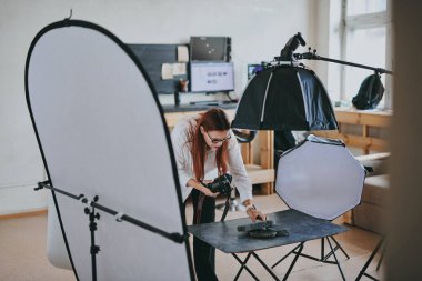 Kadın fotoğrafçı, arka plandaki objelerin fotoğrafını çekiyor. Profesyonel ekipmanlarla birlikte.