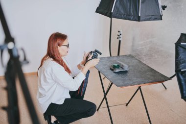 Kadın fotoğrafçı, arka plandaki objelerin fotoğrafını çekiyor. Profesyonel ekipmanlarla birlikte.