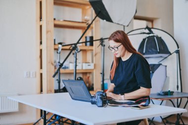 Female photographer with laptop on table processing shots in professional photo studio clipart