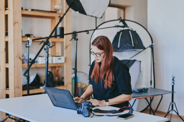 Женщина-фотограф с ноутбуком на столе обработки снимков в профессиональной фотостудии
