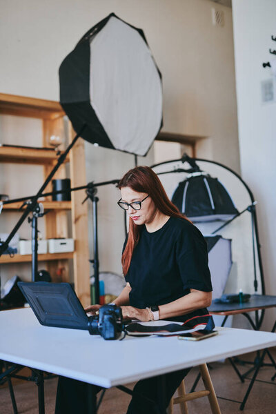 Женщина-фотограф с ноутбуком на столе обработки снимков в профессиональной фотостудии