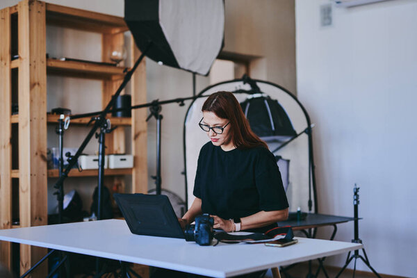 Женщина-фотограф с ноутбуком на столе обработки снимков в профессиональной фотостудии