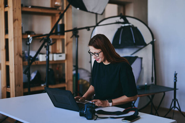 Женщина-фотограф с ноутбуком на столе обработки снимков в профессиональной фотостудии