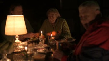 Mutlu yaşlı çift ve yetişkin kızları tatillerini evin avlusunda kutluyorlar, üç kişilik aile lamba ışığında yemek yiyorlar.