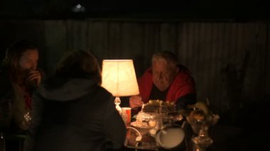 Mutlu yaşlı çift ve yetişkin kızları tatillerini evin avlusunda kutluyorlar, üç kişilik aile lamba ışığında yemek yiyorlar.