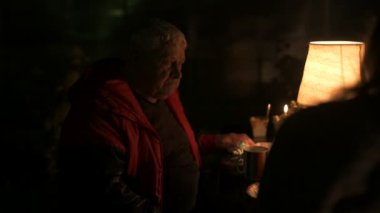 Mutlu yaşlı çift ve yetişkin kızları tatillerini evin avlusunda kutluyorlar, üç kişilik aile lamba ışığında yemek yiyorlar.