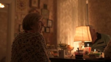 Mutlu yaşlı çift ve yetişkin kızları tatillerini masada kutluyorlar, üç kişilik aile mutfakta lamba ışığında yemek yiyorlar.