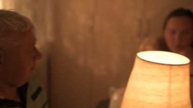 Mutlu yaşlı çift ve yetişkin kızları tatillerini masada kutluyorlar, üç kişilik aile mutfakta lamba ışığında yemek yiyorlar.