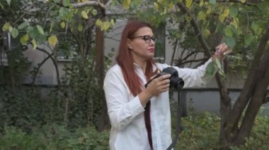 Kadın fotoğrafçı, yeşil ağaçların arka planına karşı doğada bir manzaranın fotoğraflarını çekiyor.