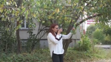 Kadın fotoğrafçı, yeşil ağaçların arka planına karşı doğada bir manzaranın fotoğraflarını çekiyor.