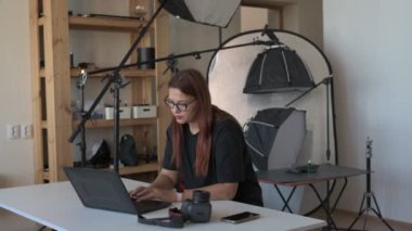Kadın fotoğrafçı, profesyonel fotoğraf stüdyosunda otururken dizüstü bilgisayardaki fotoğrafları düzenliyor.