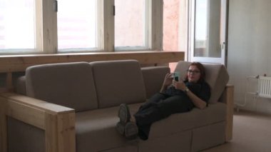 Bir kadın kanepede rahatlar ve akıllı telefon kullanarak sosyal ağlarda dolaşır.