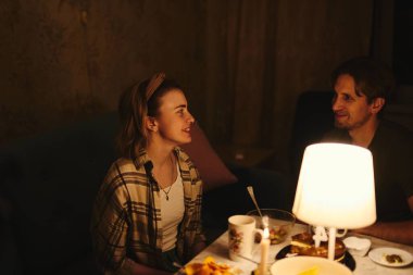 Sevgililer Günü 'nü bastırılmış sıcak aydınlatma altında, rahat evlerinde kutlayan mutlu genç çift.