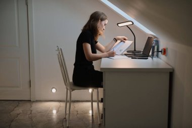 Güzel liseli kız defterleri ve ders kitaplarıyla bir masada oturur, ödevlerini yapar.