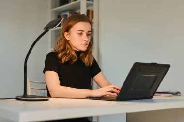 Öğrenci kız laptopla çalışıyor, daktilo ediyor ve masadaki bilgisayar ekranına bakıyor.