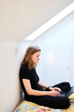 Genç öğrenci kız laptopla çalışıyor, daktilo ediyor ve yataktaki bilgisayar ekranına bakıyor.