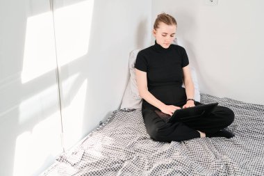 Genç öğrenci kız laptopla çalışıyor, daktilo ediyor ve yataktaki bilgisayar ekranına bakıyor.