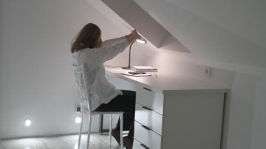 Beyaz tişörtlü liseli kız elinde not defterleri, ders kitapları, akıllı telefon ve dizüstü bilgisayarla masada oturuyor, ödev yapıyor, internetten öğrenim görüyor.