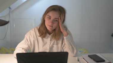 Beyaz tişörtlü liseli kız elinde not defterleri, ders kitapları, akıllı telefon ve dizüstü bilgisayarla masada oturuyor, ödev yapıyor, internetten öğrenim görüyor.