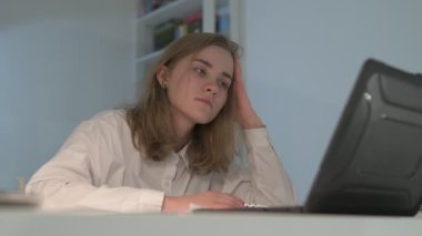 Beyaz tişörtlü liseli kız elinde not defterleri, ders kitapları, akıllı telefon ve dizüstü bilgisayarla masada oturuyor, ödev yapıyor, internetten öğrenim görüyor.