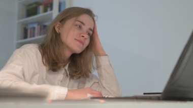 Beyaz tişörtlü liseli kız elinde not defterleri, ders kitapları, akıllı telefon ve dizüstü bilgisayarla masada oturuyor, ödev yapıyor, internetten öğrenim görüyor.