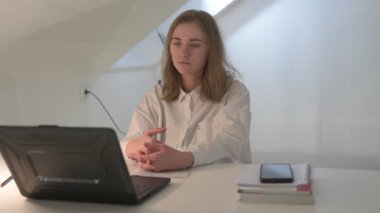 Beyaz tişörtlü liseli kız elinde not defterleri, ders kitapları, akıllı telefon ve dizüstü bilgisayarla masada oturuyor, ödev yapıyor, internetten öğrenim görüyor.