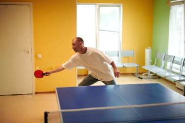 Beyaz tişörtlü bir adam masa tenisi oynamaktan hoşlanır. Pinpon kulübünde dostça bir rekabet.