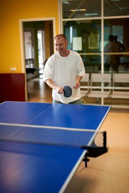 Beyaz tişörtlü bir adam masa tenisi oynamaktan hoşlanır. Pinpon kulübünde dostça bir rekabet.