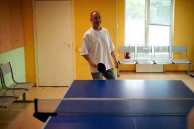 Beyaz tişörtlü bir adam masa tenisi oynamaktan hoşlanır. Pinpon kulübünde dostça bir rekabet.